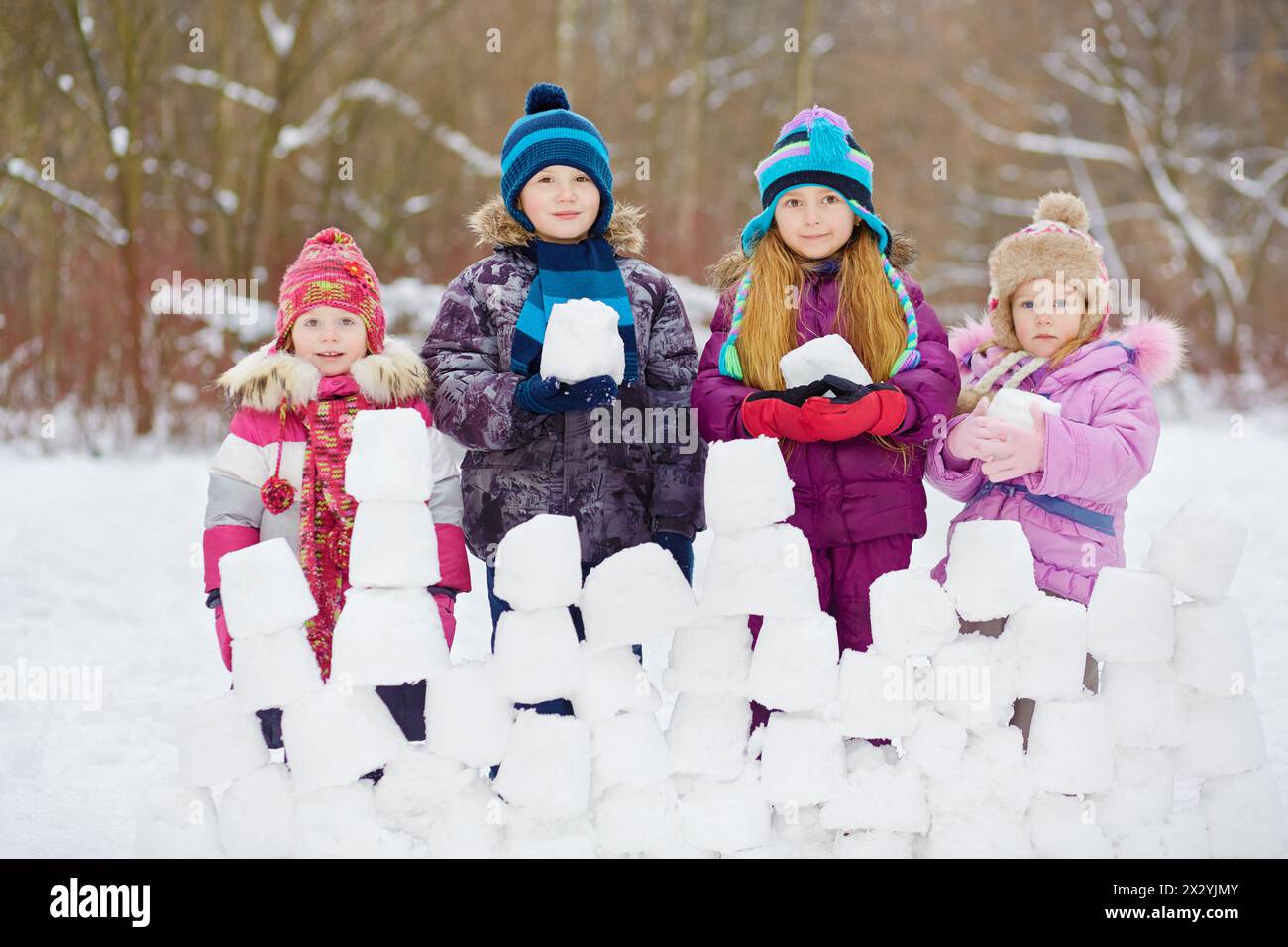 Les enfants se tiennent derrière le mur de neige tenant des blocs de neige, hiver, parc Banque D'Images