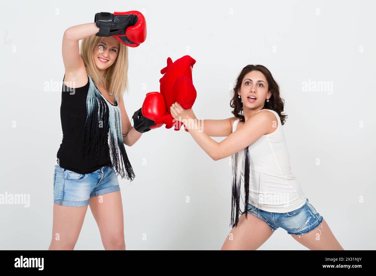 Deux jolies filles en short en denim s'amusant, une avec des gants de boxe l'autre avec un coussin en forme de coeur Banque D'Images