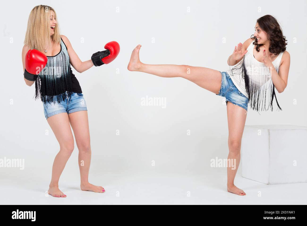 Deux filles mignonnes en short en denim s'amusant, une avec des gants de boxe d'autres baskets Banque D'Images
