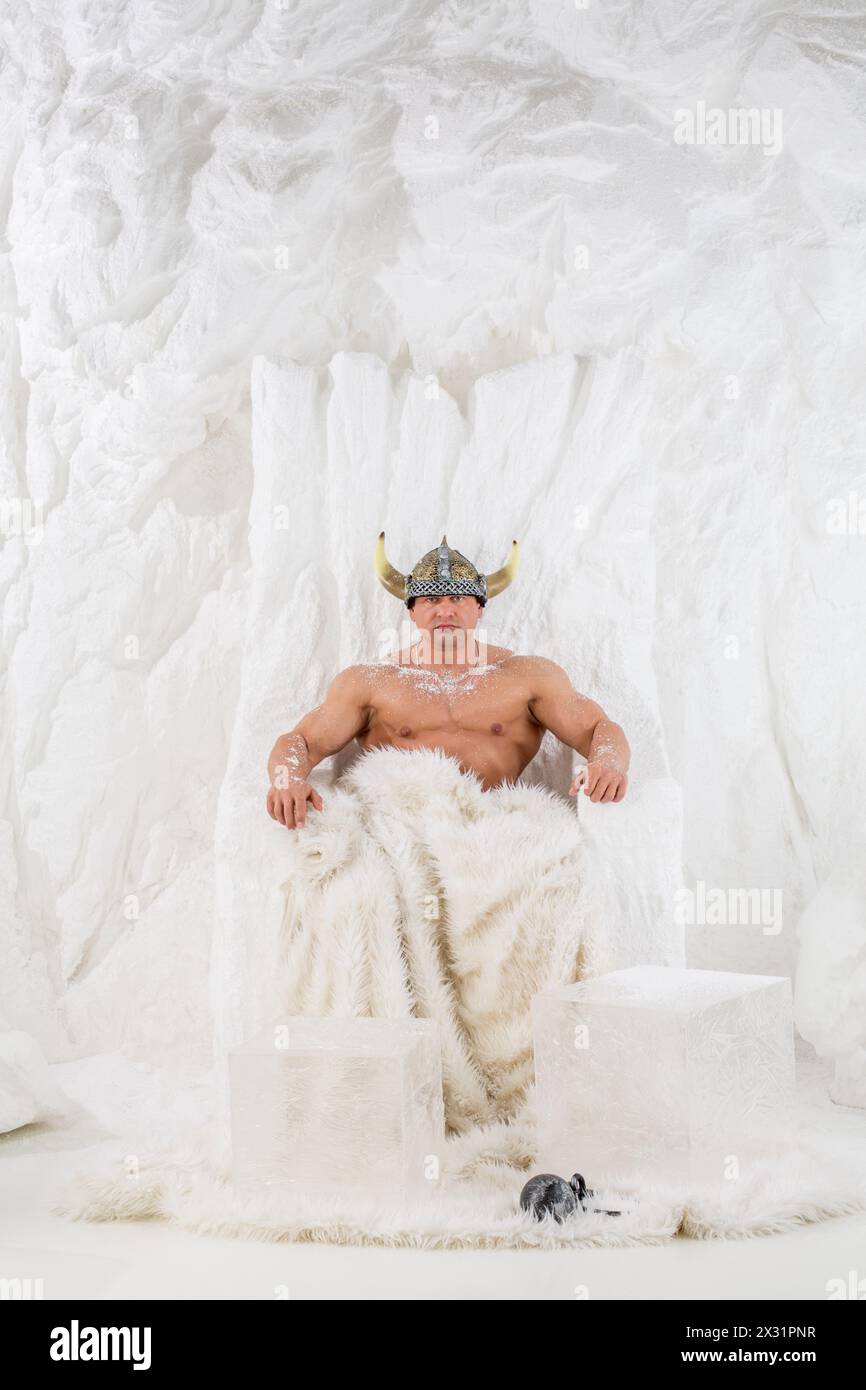 Un homme musclé dans le casque viking avec de la neige sur le corps assis dans la chaise de neige Banque D'Images