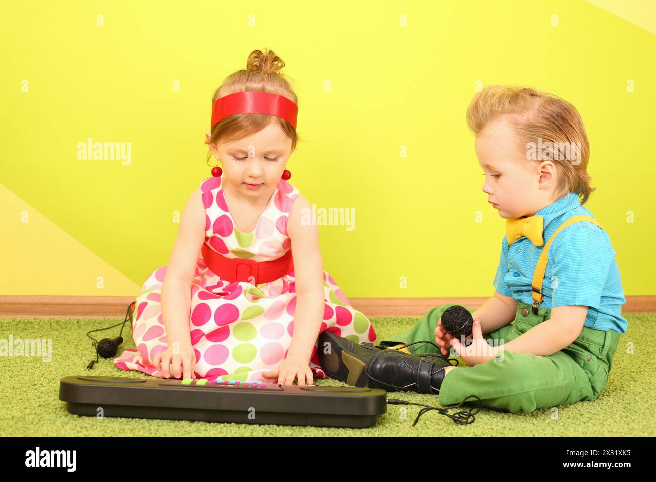 Mods garçon et fille dans des vêtements lumineux assis sur le sol devant un piano jouet Banque D'Images