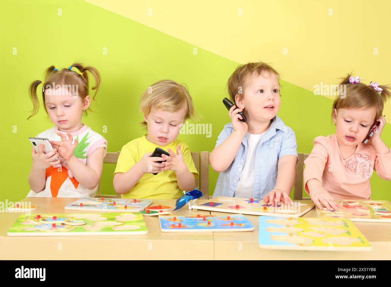 Deux garçons et deux filles avec des téléphones dans les mains sont assis à une table avec des jouets Banque D'Images
