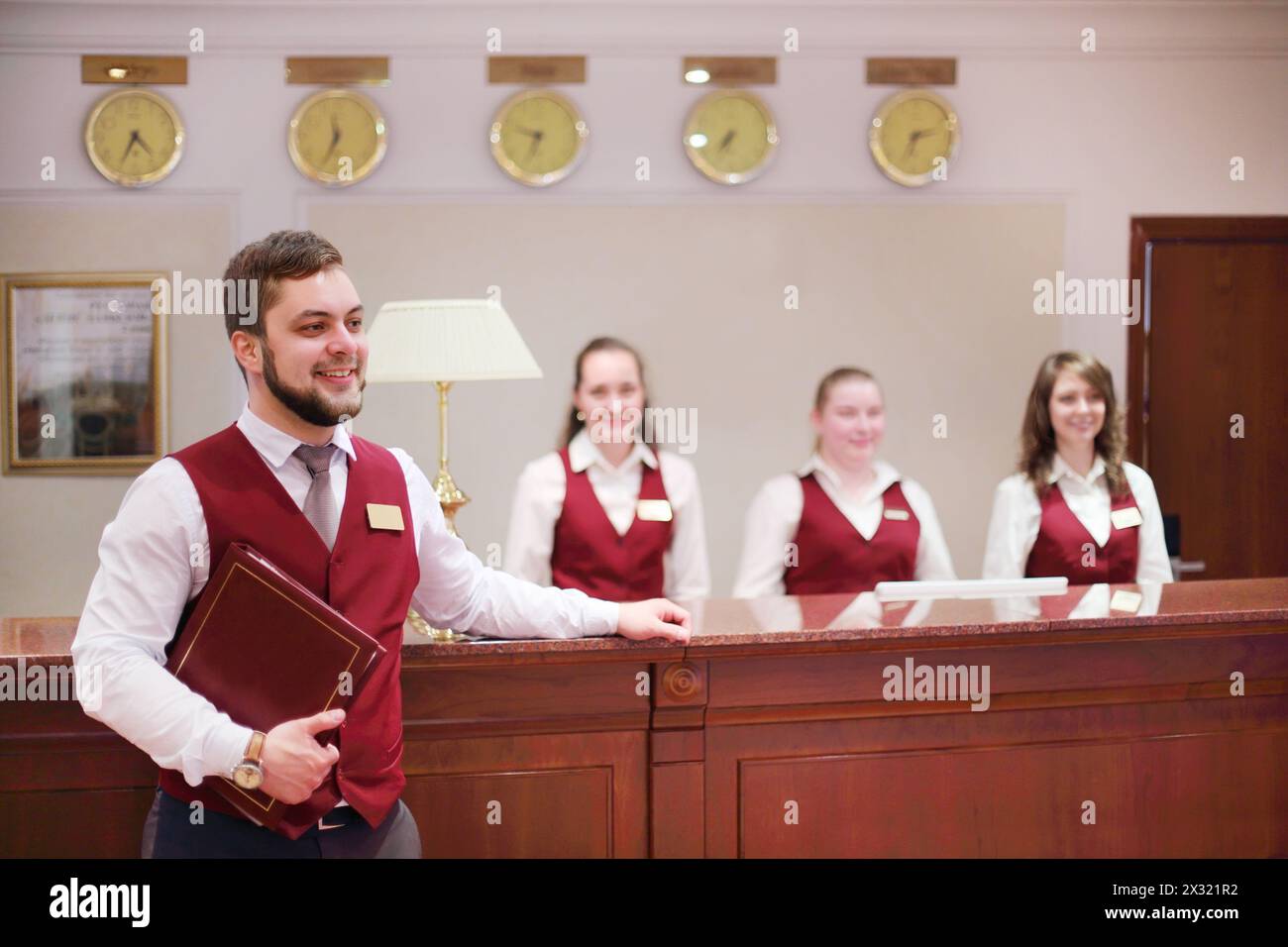 Heureux réceptionnistes - un homme, trois femmes au comptoir pour les clients à l'hôtel, Banque D'Images