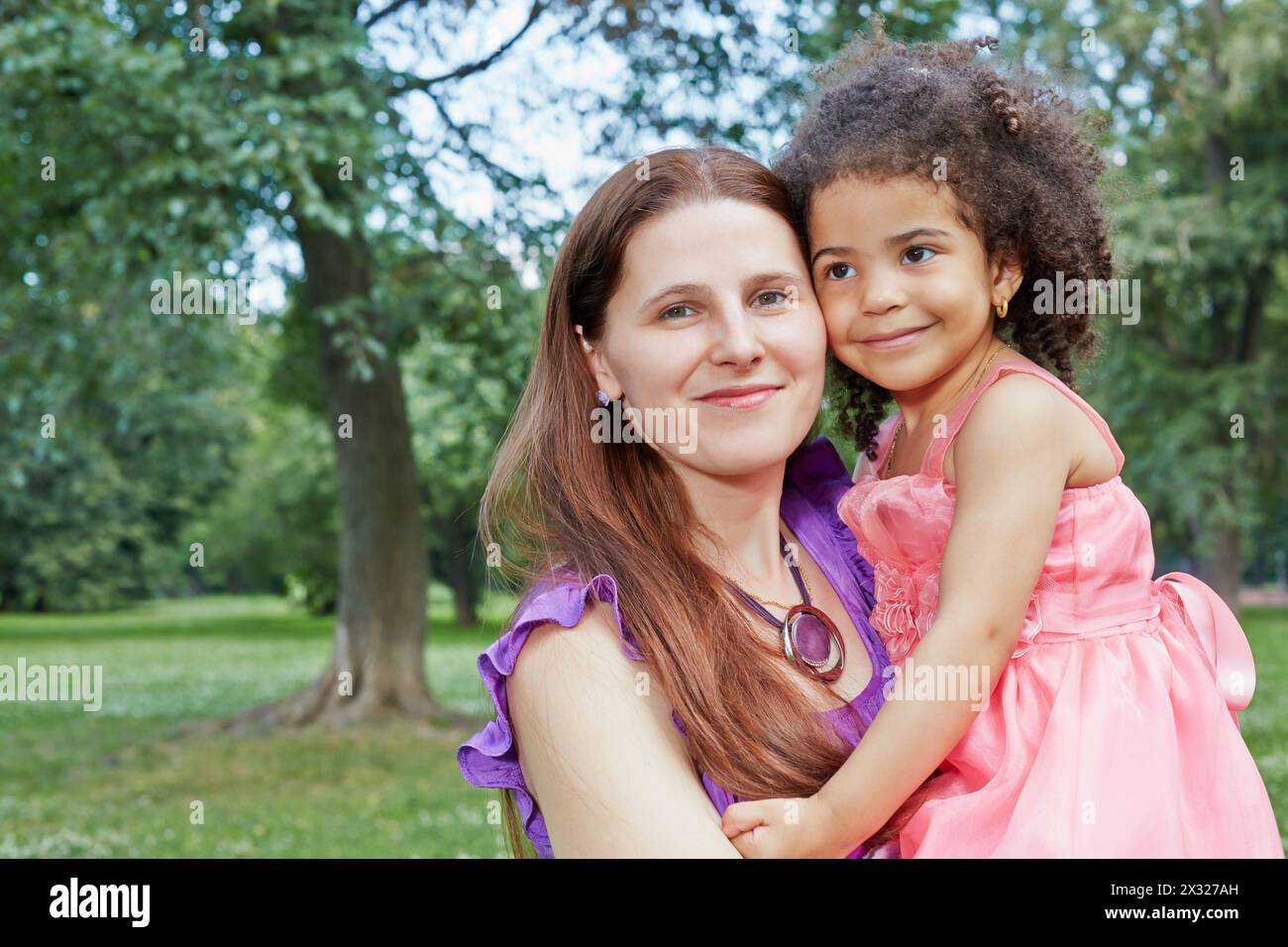 Gros plan portrait de mère qui tient sa petite fille dans ses bras, debout dans le parc le jour d'été Banque D'Images