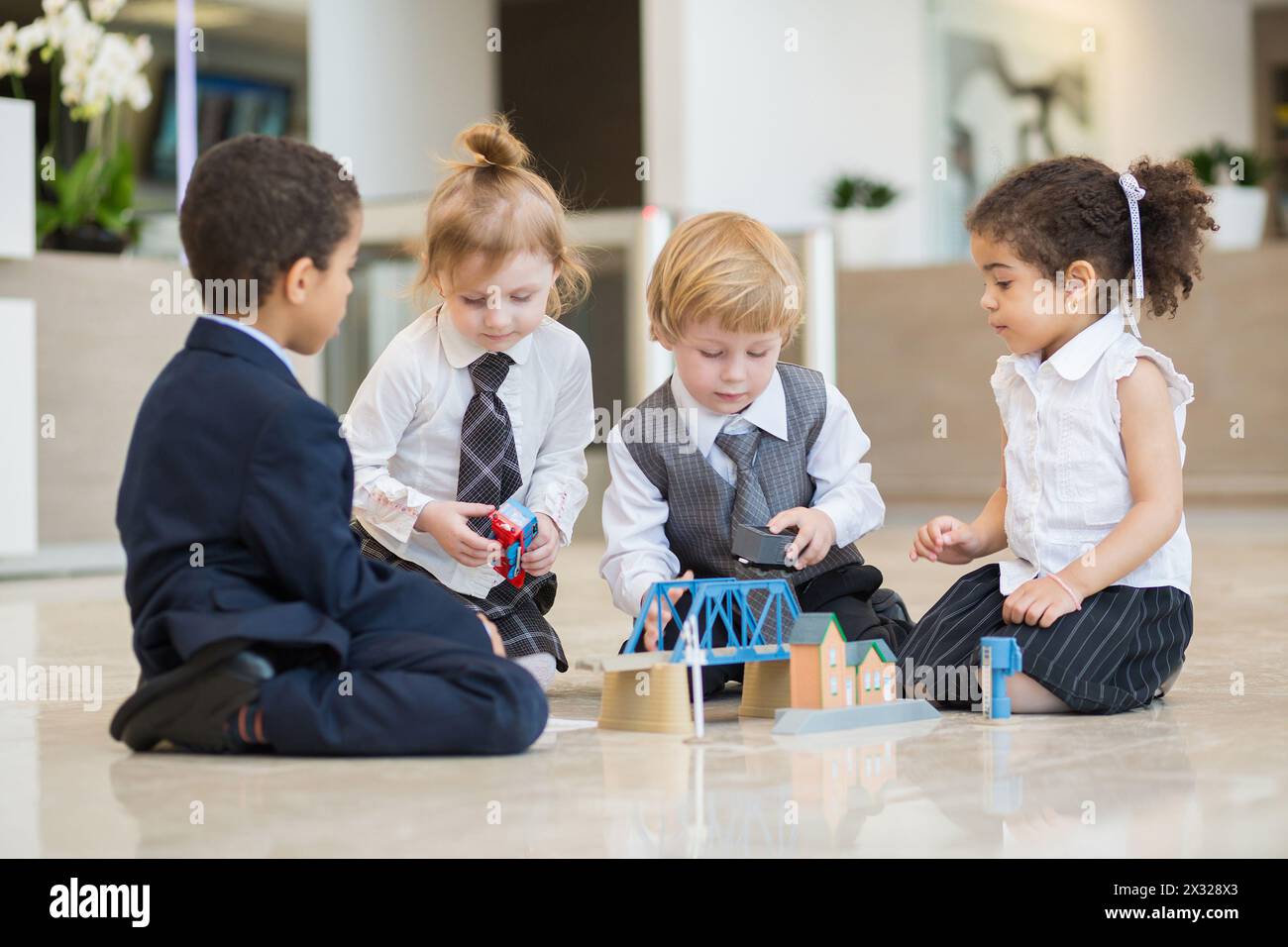 Quatre enfants en tenue d'affaires jouant avec des jouets dans le centre d'affaires Banque D'Images