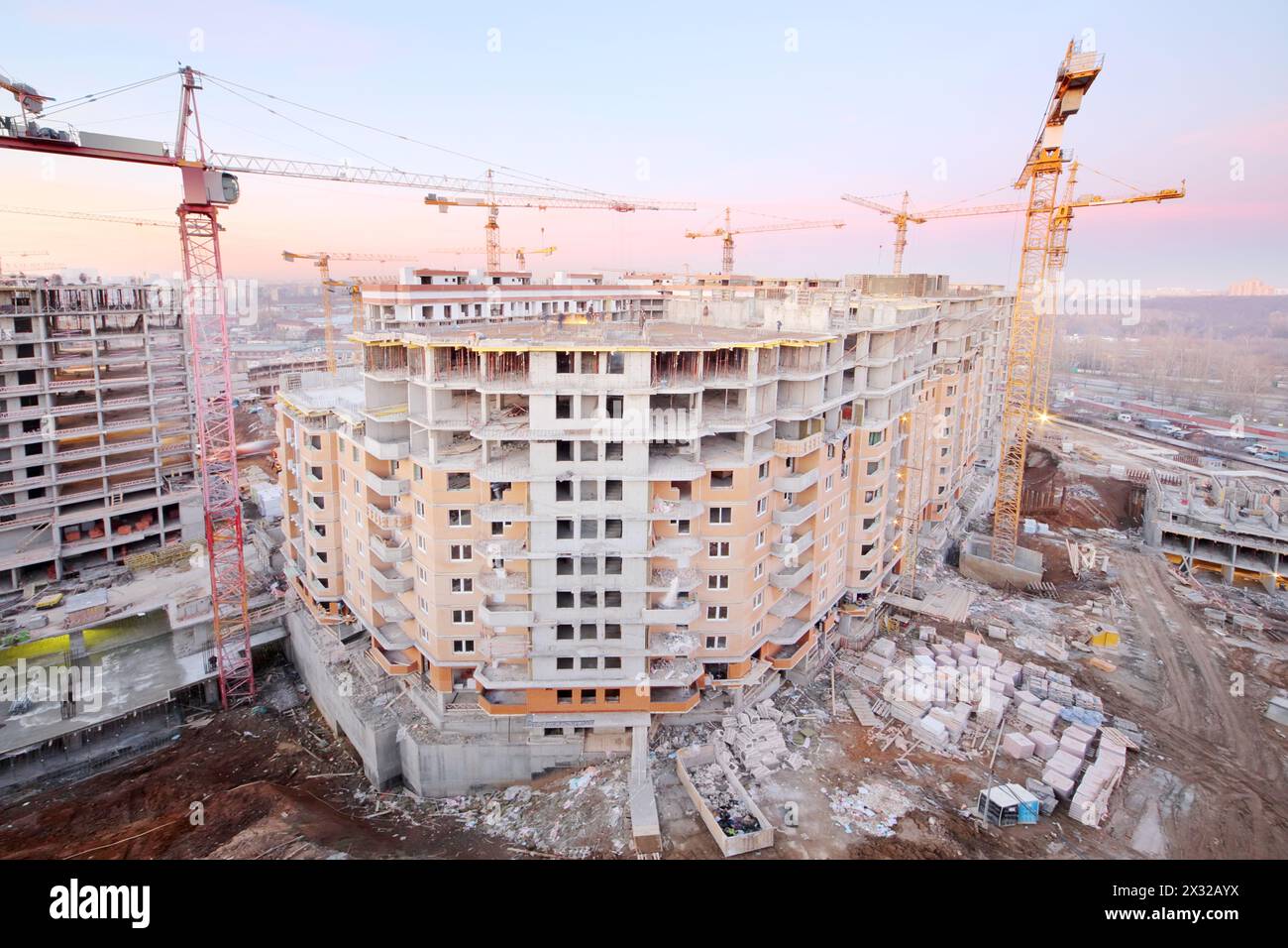 Beaucoup de grues à tour construisent un grand bâtiment résidentiel le soir. Banque D'Images