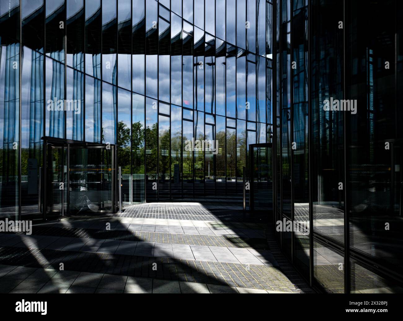 Danse de lumière et d'ombre à travers la façade vitrée de la Tour Post à Bonn : des reflets captivants alors que l'architecture moderne rencontre la beauté de la nature. Banque D'Images