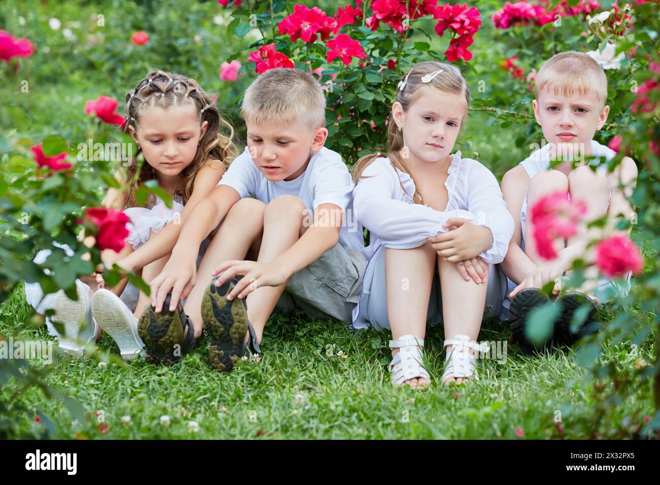Les enfants sont assis sur l'herbe parmi les fleurs dans le jardin Banque D'Images