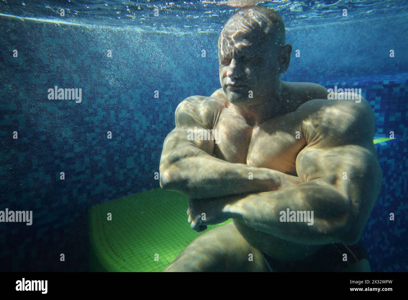 Bodybuilder avec les yeux fermés dans la piscine sous l'eau parmi de nombreuses petites bulles Banque D'Images