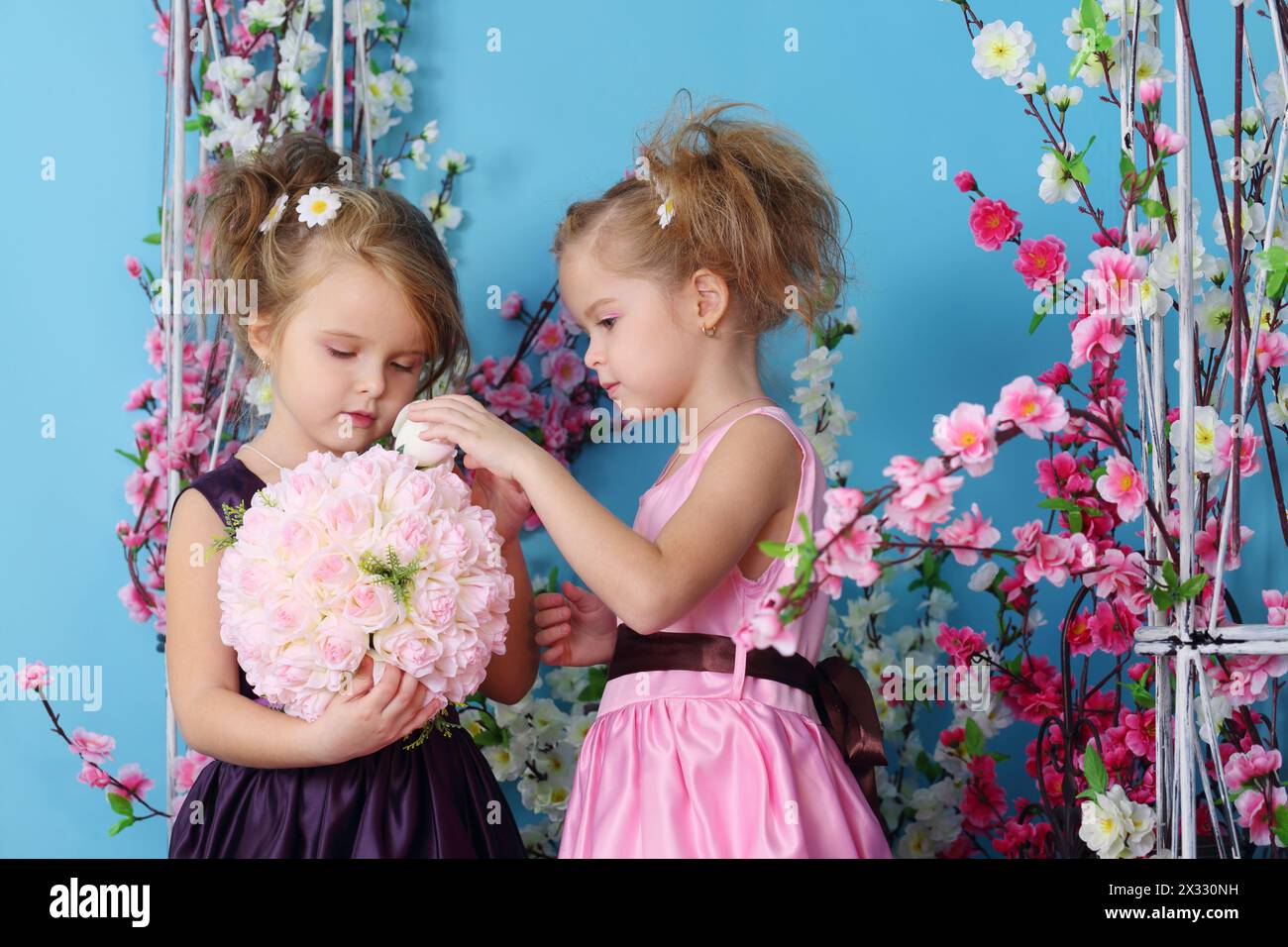 Deux petites filles mignonnes en robes composent bouquet de roses dans la chambre avec des fleurs. Banque D'Images