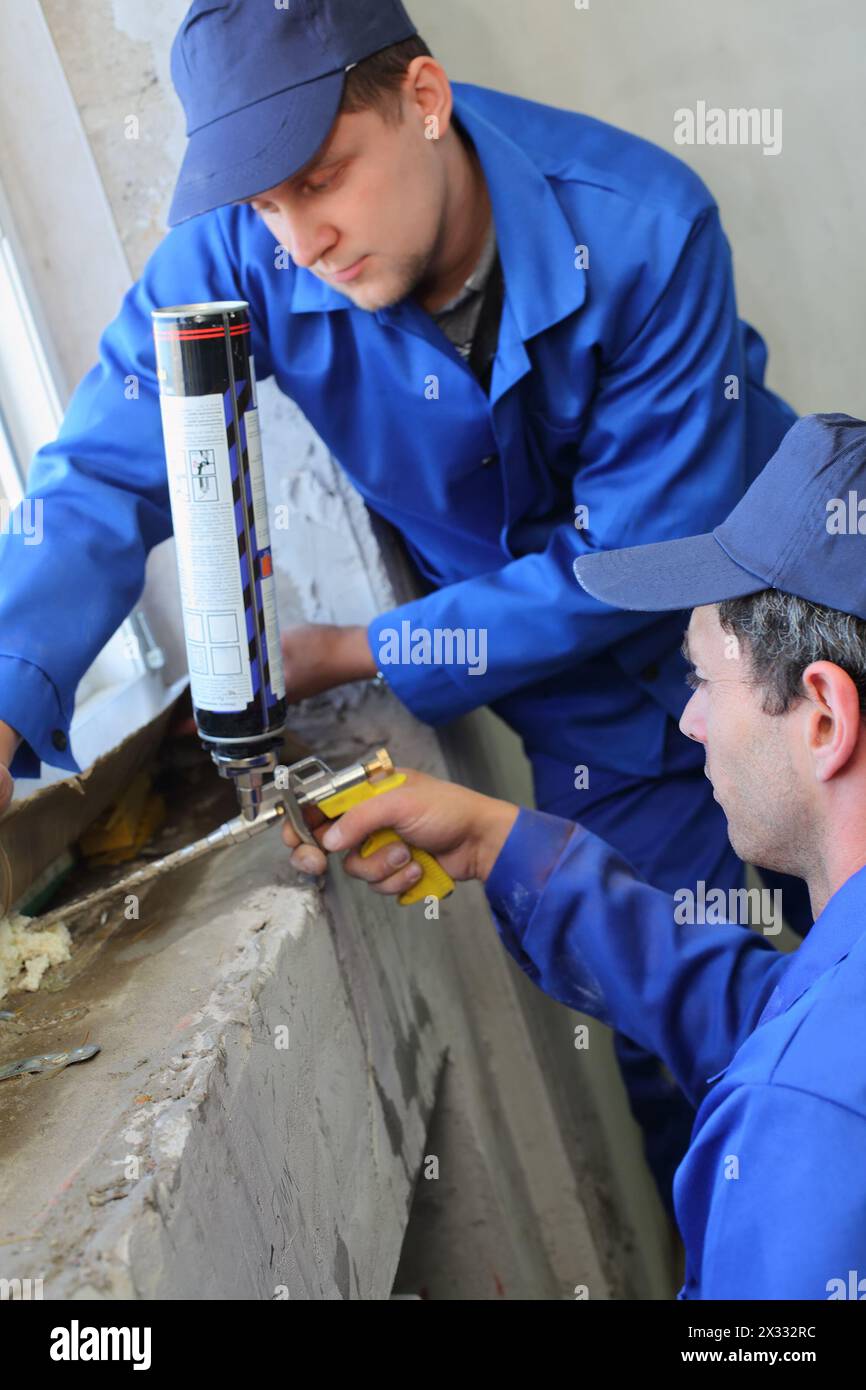 Deux hommes en vêtements de travail ont utilisé la mousse de montage pour l'isolation thermique de la fenêtre Banque D'Images