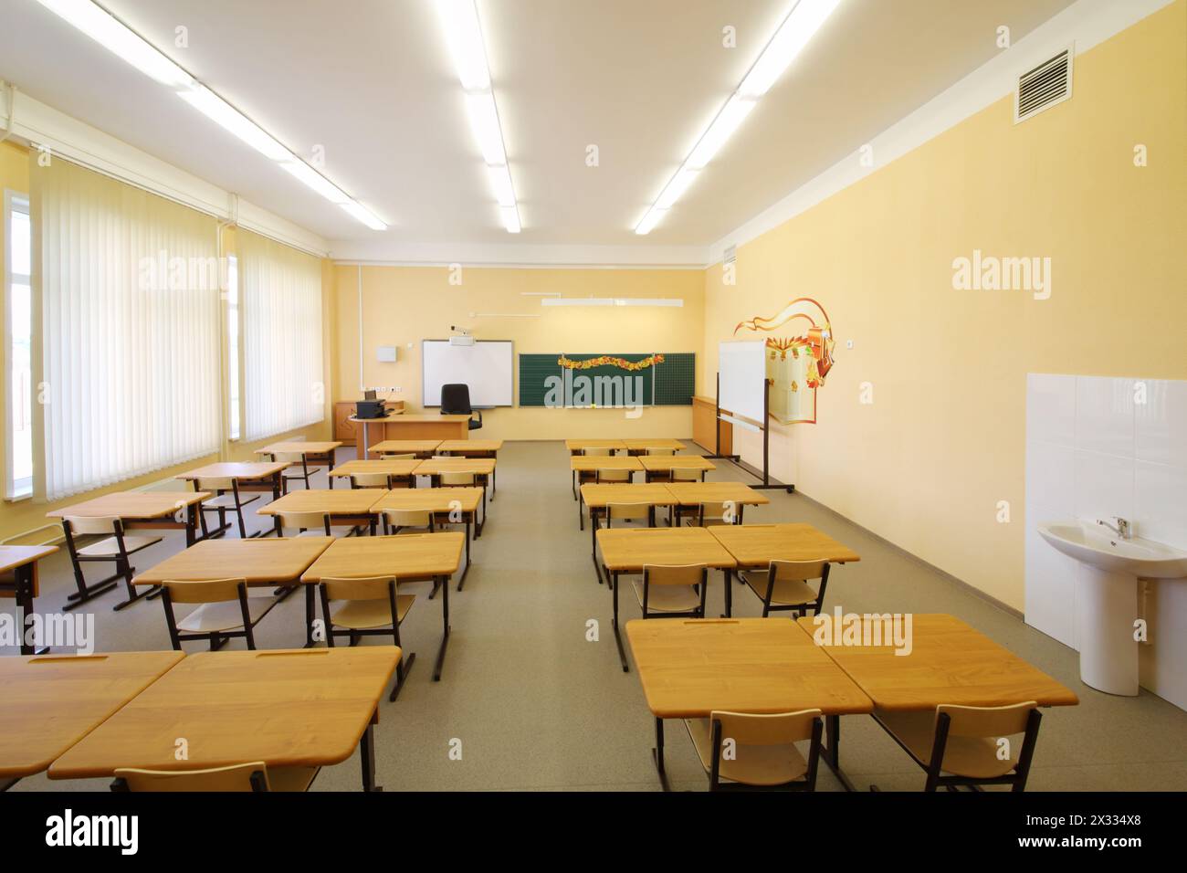 Salle de classe vide avec des bureaux en bois, un tableau de craie et des murs jaunes à l'école. Banque D'Images