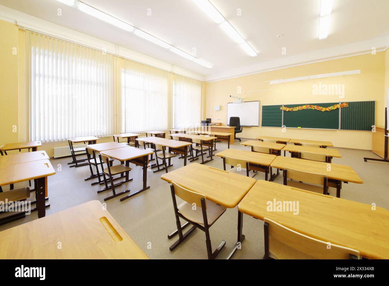 Salle de classe vide avec des bureaux en bois, un tableau de craie et de grandes fenêtres à l'école. Banque D'Images