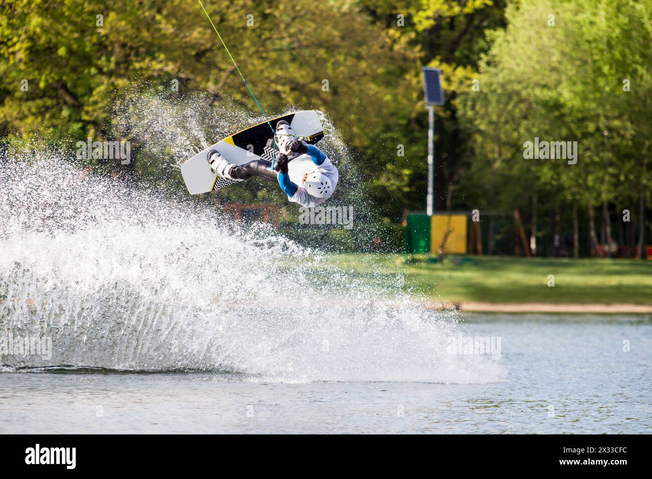 Le wakeboarder mâle saute par-dessus la pulvérisation sur l'étang dans le parc Banque D'Images