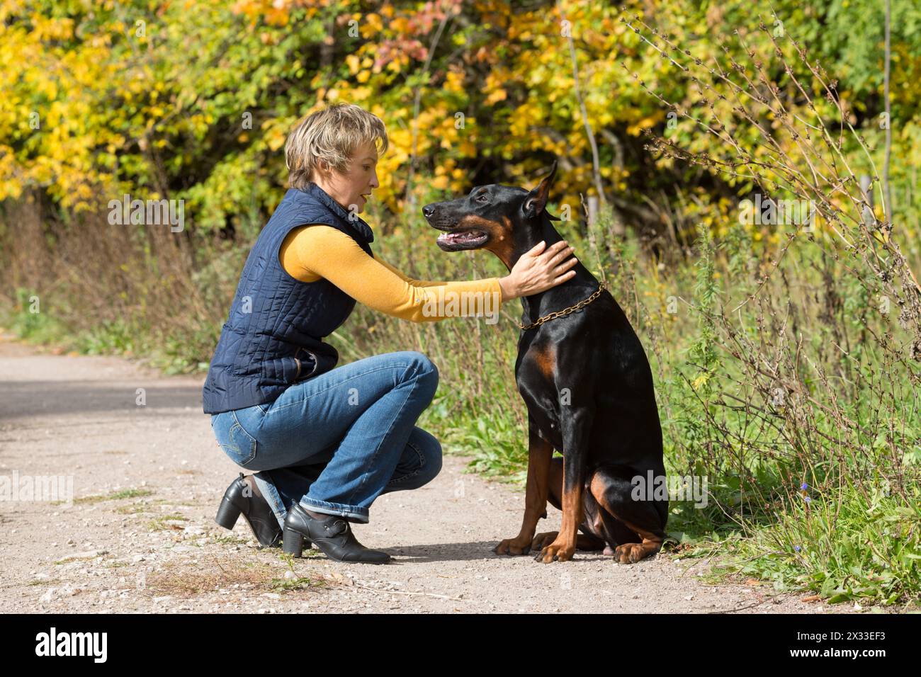Femme au col polo beige est assise devant le chien noir dans un parc. Banque D'Images