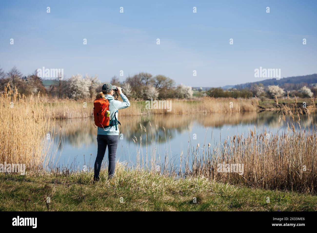 Tourisme écologique. Femme randonneur avec des jumelles observant les oiseaux et les animaux sauvages au lac. Randonnée et observation des oiseaux dans la nature printanière Banque D'Images