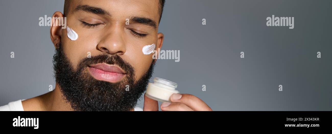 Beau jeune homme afro-américain appliquant de la crème sur son visage. Banque D'Images