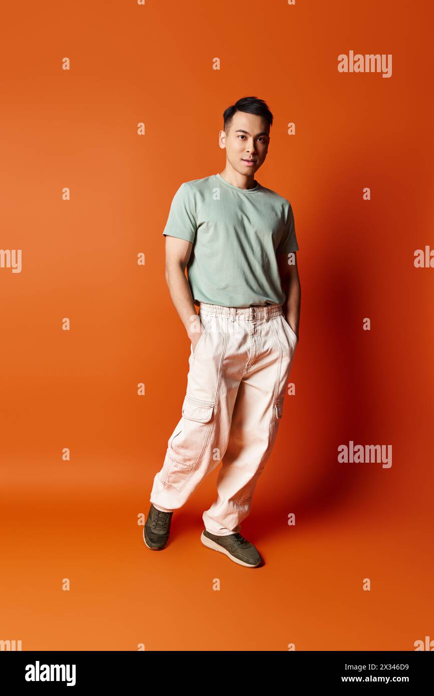 Un bel homme asiatique dans une tenue élégante se tient confiant devant un fond orange vif, exsudant sophistication et calme. Banque D'Images