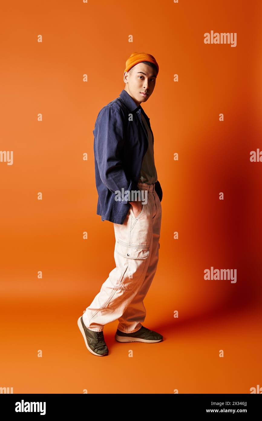 Un bel homme asiatique se tient confiant dans une tenue élégante sur un fond orange vif dans un cadre de studio. Banque D'Images