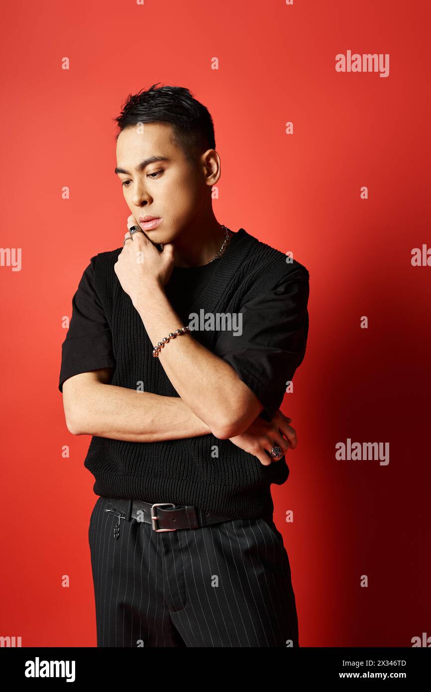 Bel homme asiatique en chemise noire se tient confiant contre fond rouge vif dans le cadre de studio. Banque D'Images