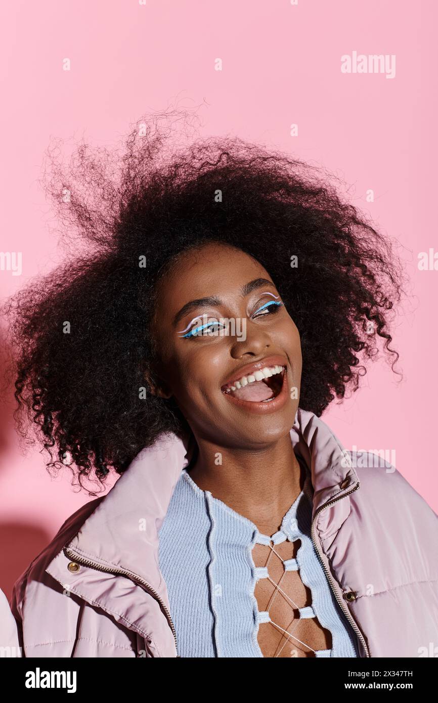 Une jeune femme afro-américaine élégante aux cheveux bouclés sourit brillamment dans un cadre de studio, exsudant confiance et joie. Banque D'Images