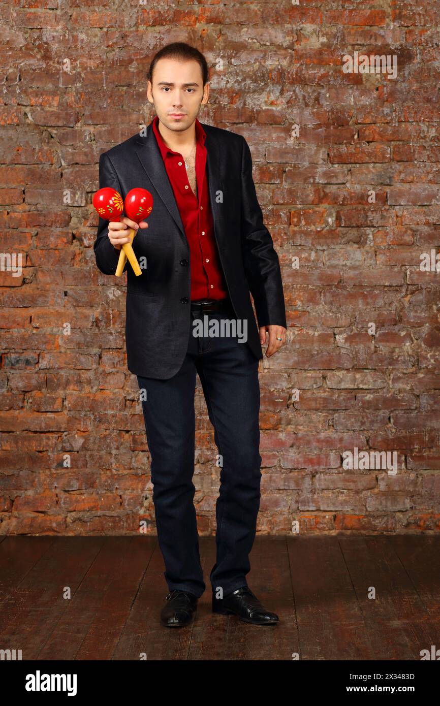 Jeune homme en costume se dresse avec des maracas en studio avec mur de briques Banque D'Images
