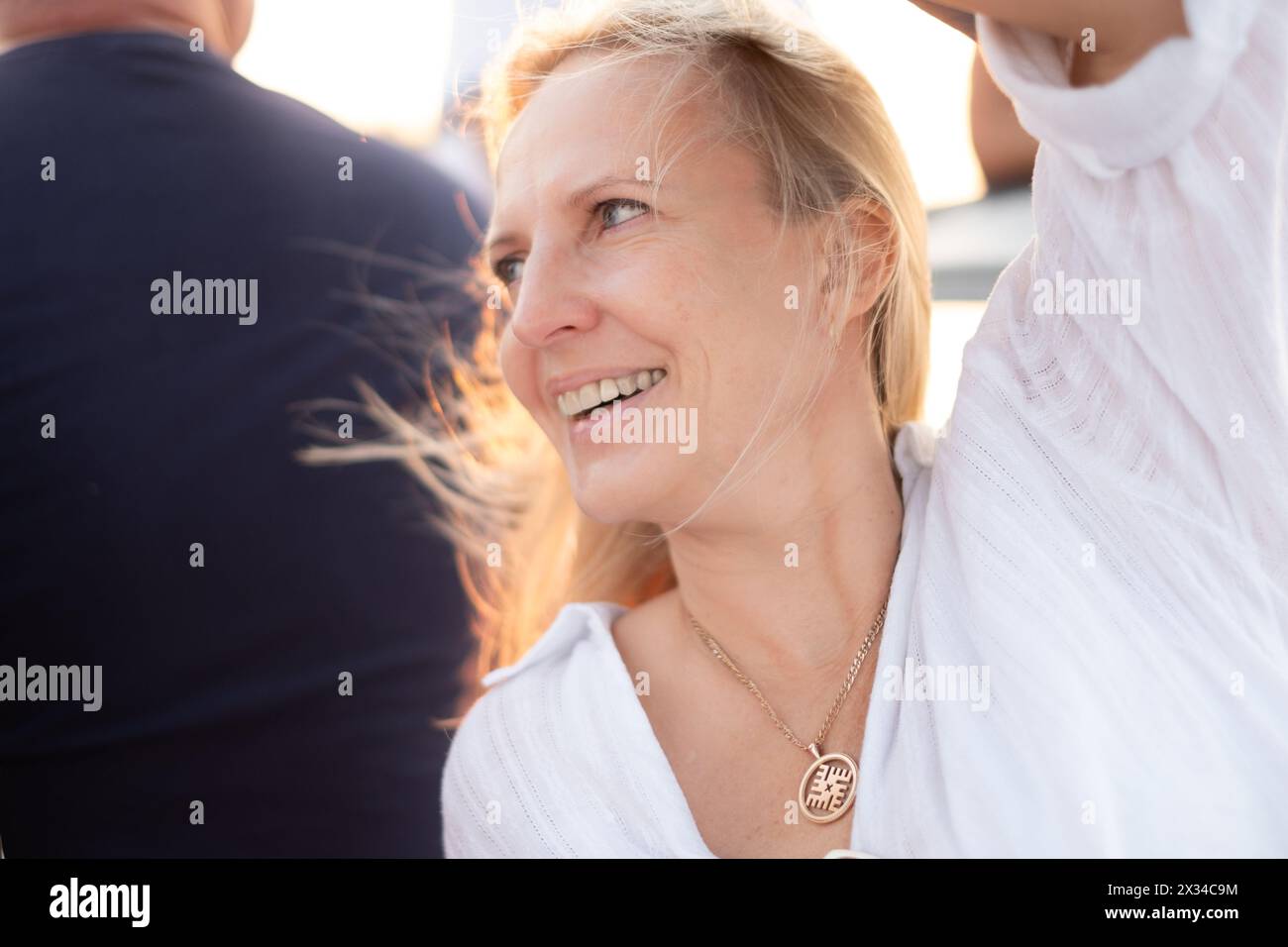 Sourire radieux d'une femme jouissant d'une lueur d'heure dorée, la joie du moment illuminant son expression au milieu d'un rassemblement animé. Photo de haute qualité Banque D'Images