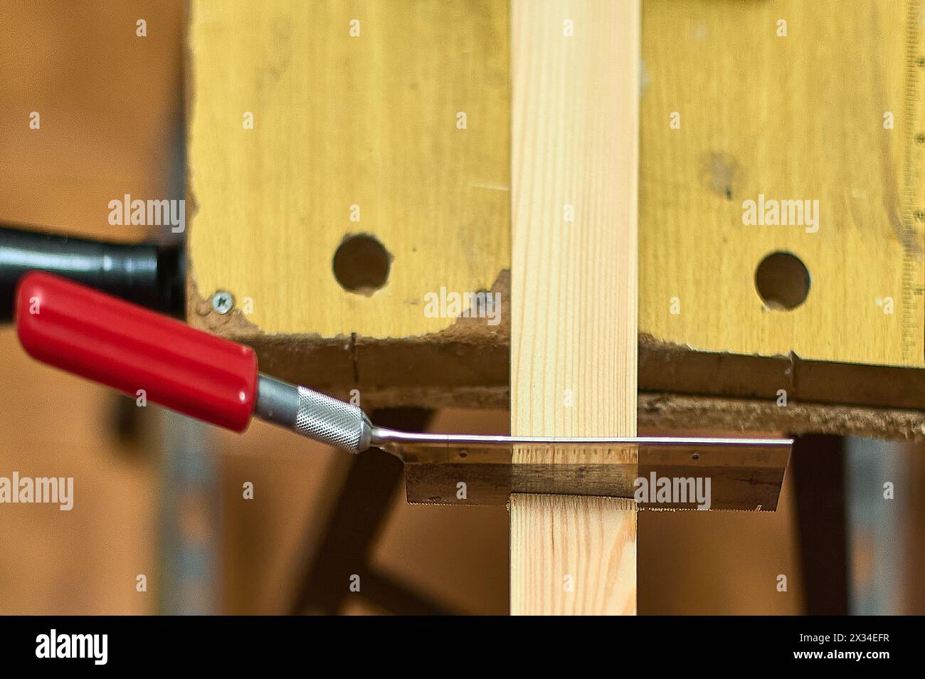 Gros plan d'une scie coupant une planche de bois dans un atelier de menuiserie, mettant en valeur la précision et l'habileté dans le travail manuel. Banque D'Images