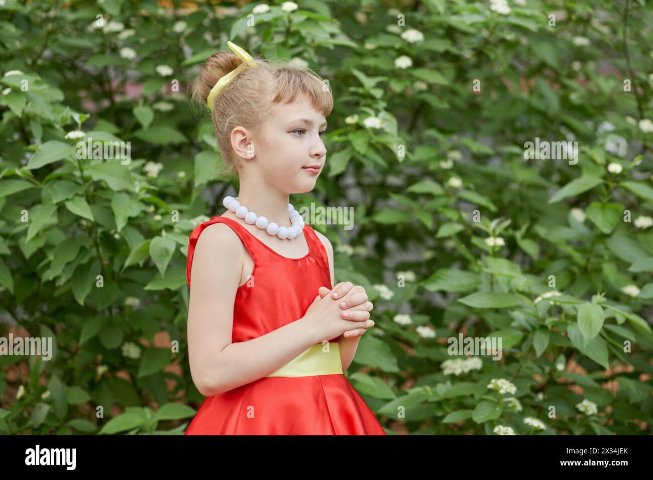 Portrait mi-long de la petite fille vêtue d'une robe rouge avec collier de grosses perles blanches debout à l'extérieur. Banque D'Images