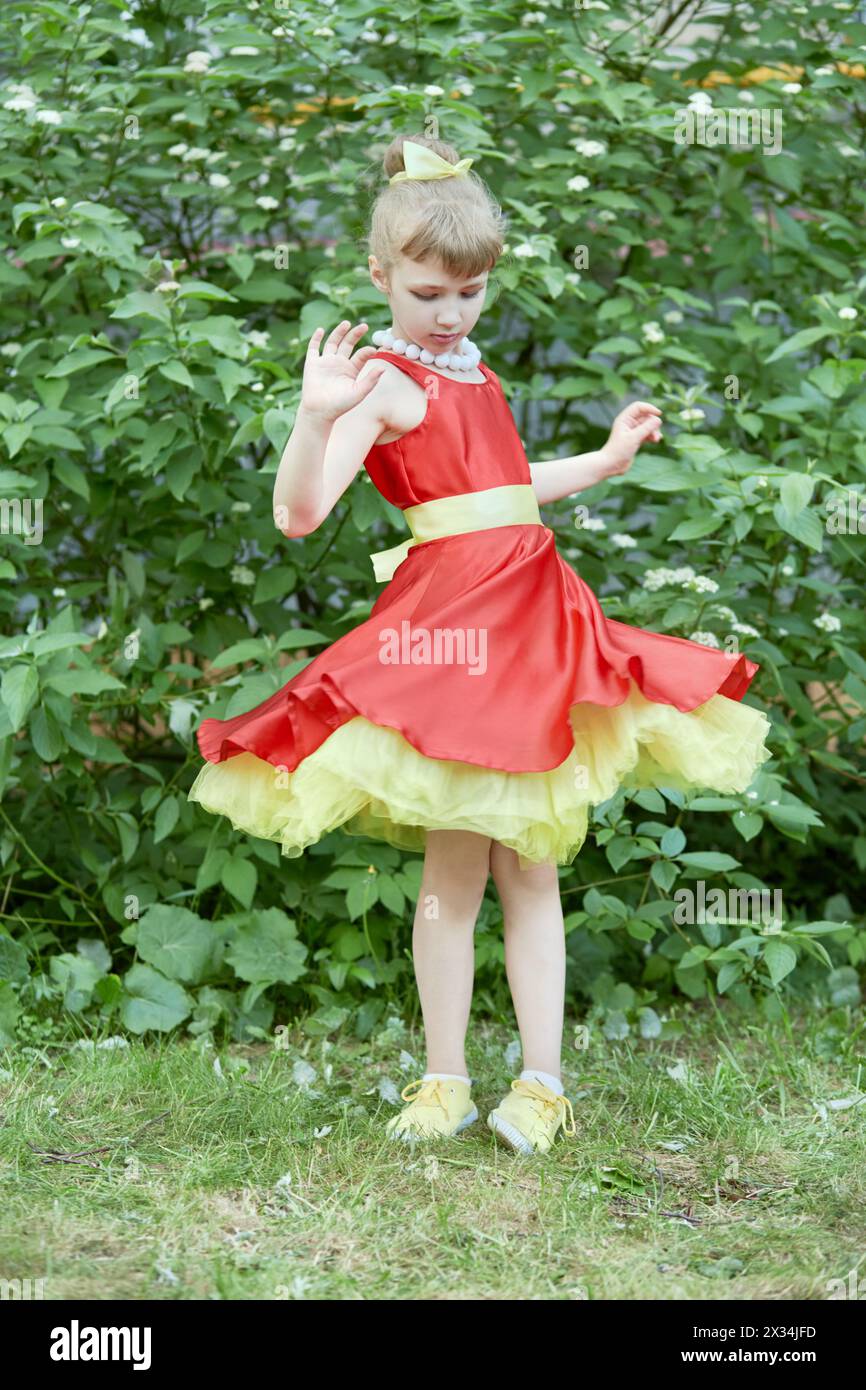 Petite fille vêtue d'une robe rouge avec sous-jupe jaune spins debout à l'extérieur. Banque D'Images