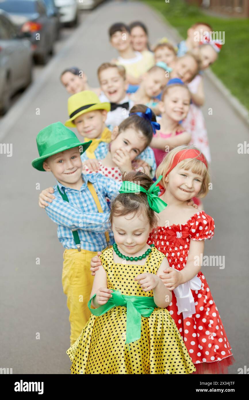 Quinze enfants se tiennent debout un par un en se pliant aux côtés défférents sur le trottoir, se concentrer sur la première fille. Banque D'Images