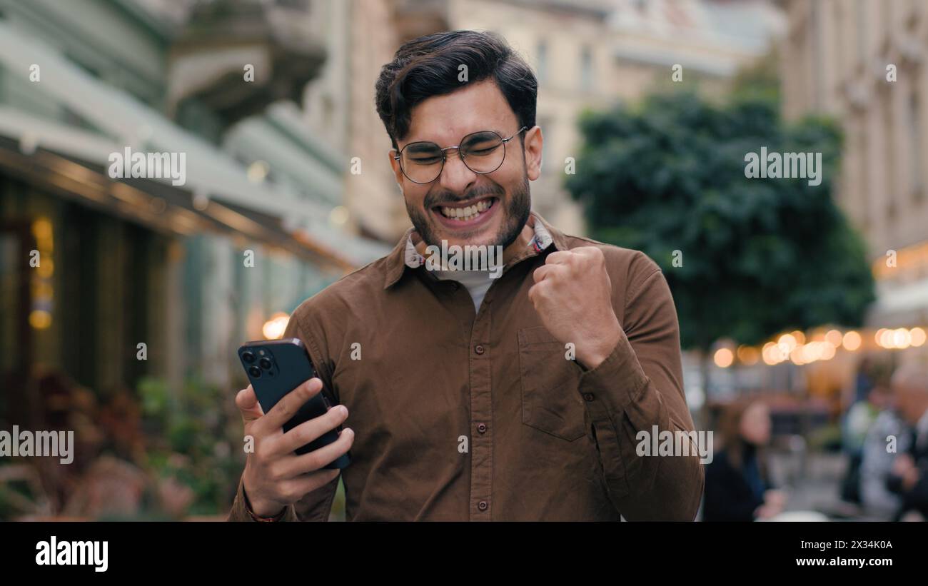 Heureux espoir heureux Indien arabe heureux homme ethnique homme d'affaires homme d'affaires homme jeune étudiant de sexe masculin tenir téléphone mobile smartphone souhaitant espoir prier les doigts croisés Banque D'Images