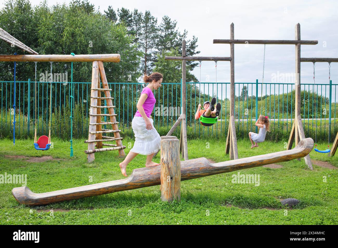 Mère avec fils et fille se balançant sur une balançoire sur une aire de jeux en bois Banque D'Images