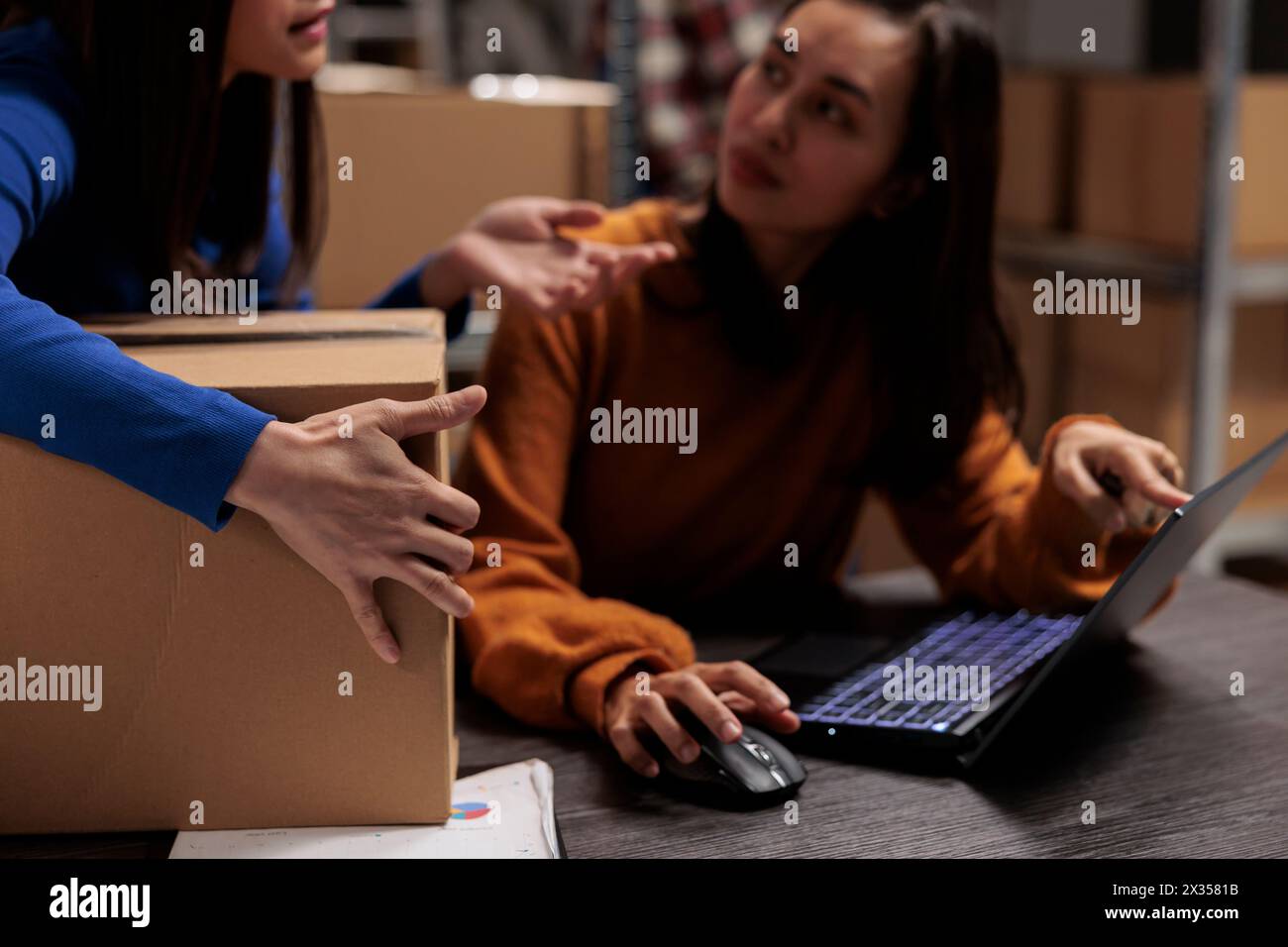 Employé de Storehouse demandant à un collègue sur le ticket de cueillette sur ordinateur portable tout en travaillant au bureau dans la salle de stockage d'entreprise de commerce de détail en ligne. Collègues qui suivent l'expédition des colis et préparent la boîte pour l'expédition Banque D'Images