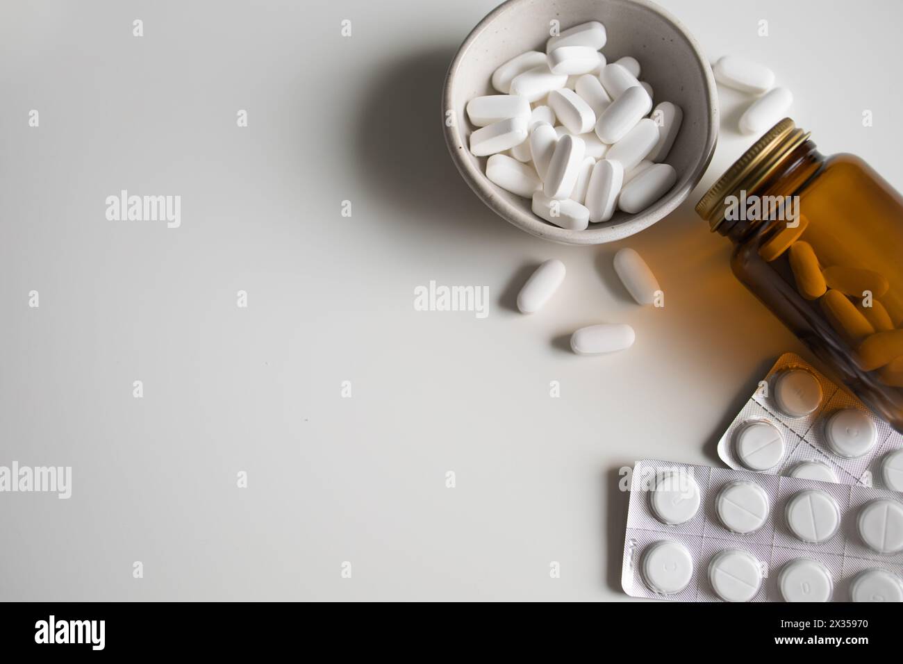 Pilules blanches dans un bol, renversé de la bouteille et comprimés blancs dans des plaquettes thermoformées sur fond blanc Banque D'Images