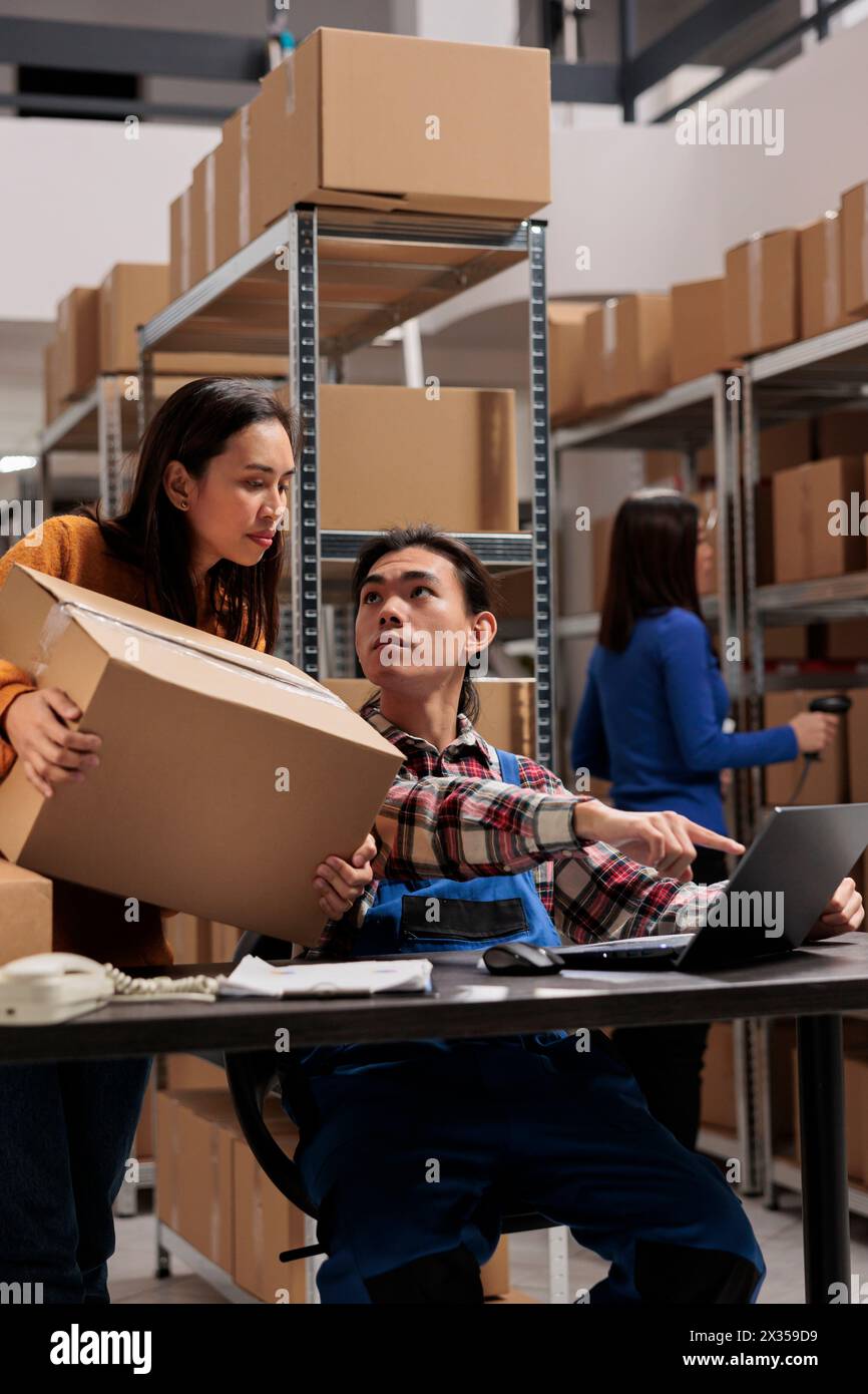 Entrepôt travailleurs asiatiques tenant le colis et planifiant la livraison sur ordinateur portable. Les employés du magasin discutent de la liste de contrôle des commandes et analysent le ticket de cueillette sur ordinateur dans la salle de stockage Banque D'Images