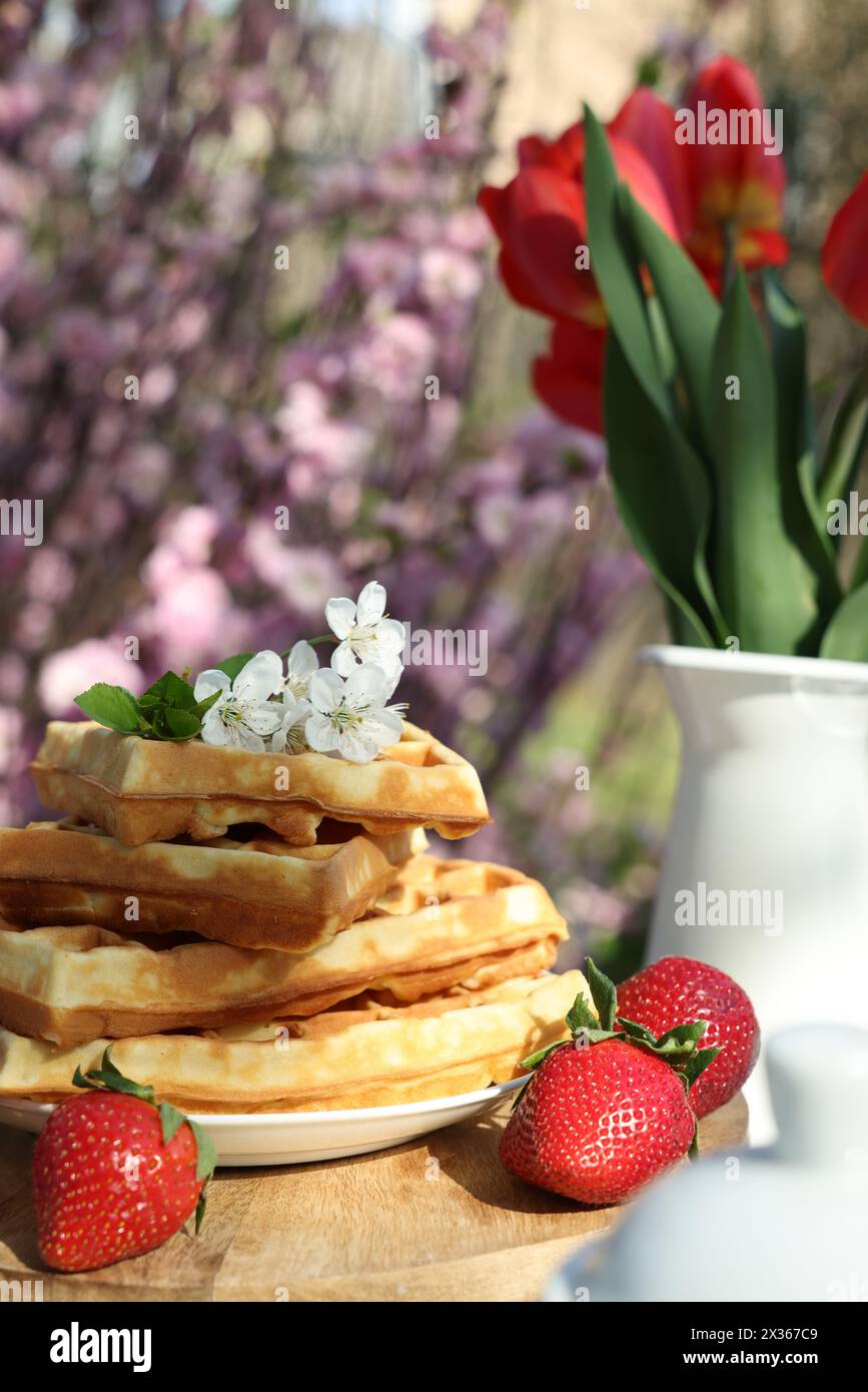Gaufres fraîchement cuites et beau bouquet de tulipes sur table dans le jardin, gros plan Banque D'Images