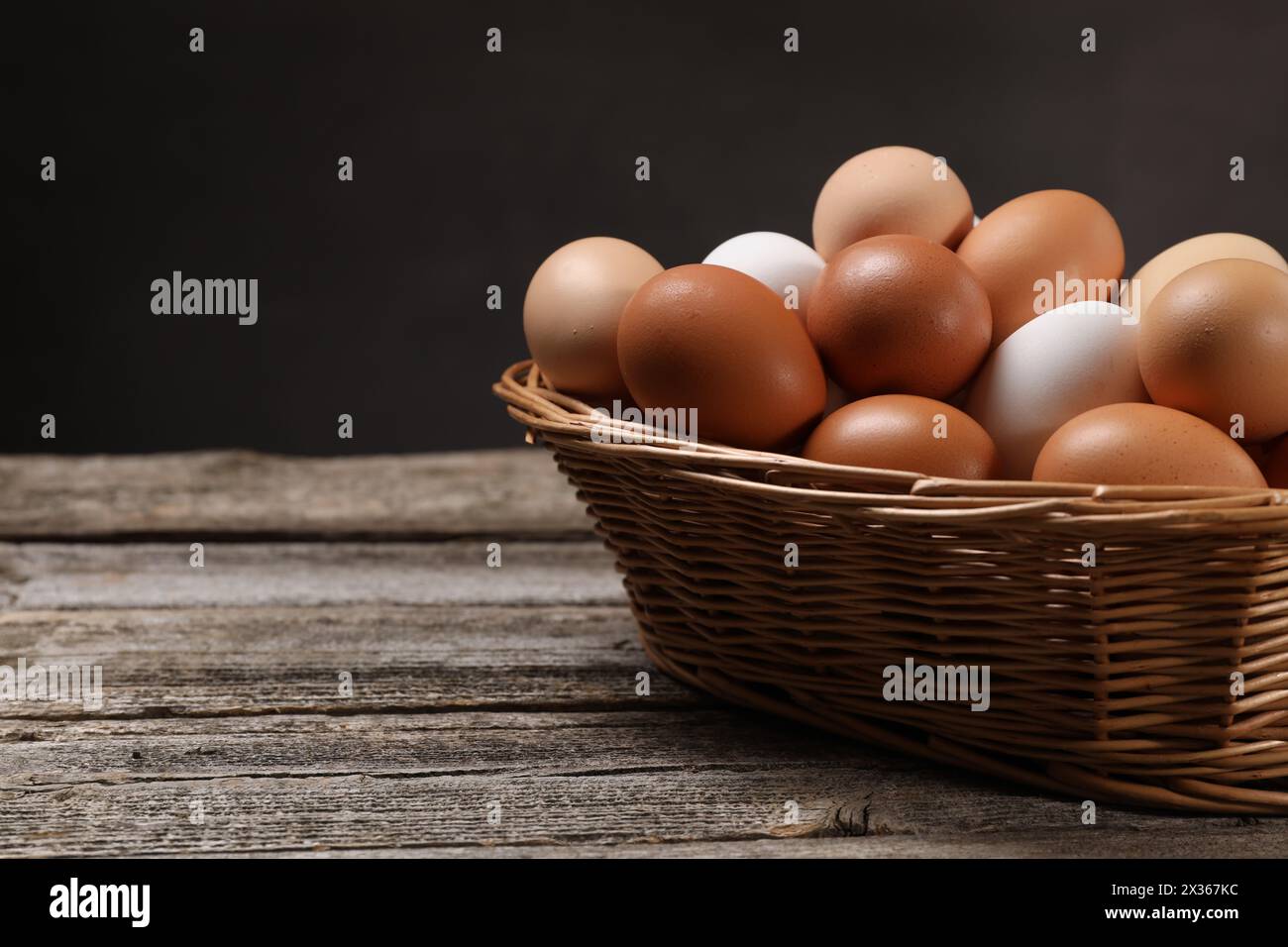 Oeufs de poule frais dans un panier en osier sur une table en bois. Espace pour le texte Banque D'Images