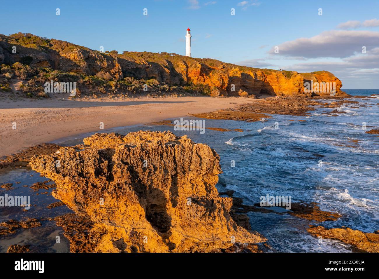 Vue lointaine d'un phare blanc sur des falaises érodées au-dessus d'une côte accidentée à Aireys Inlet sur la Great Ocean Road à Victoria, Australie Banque D'Images