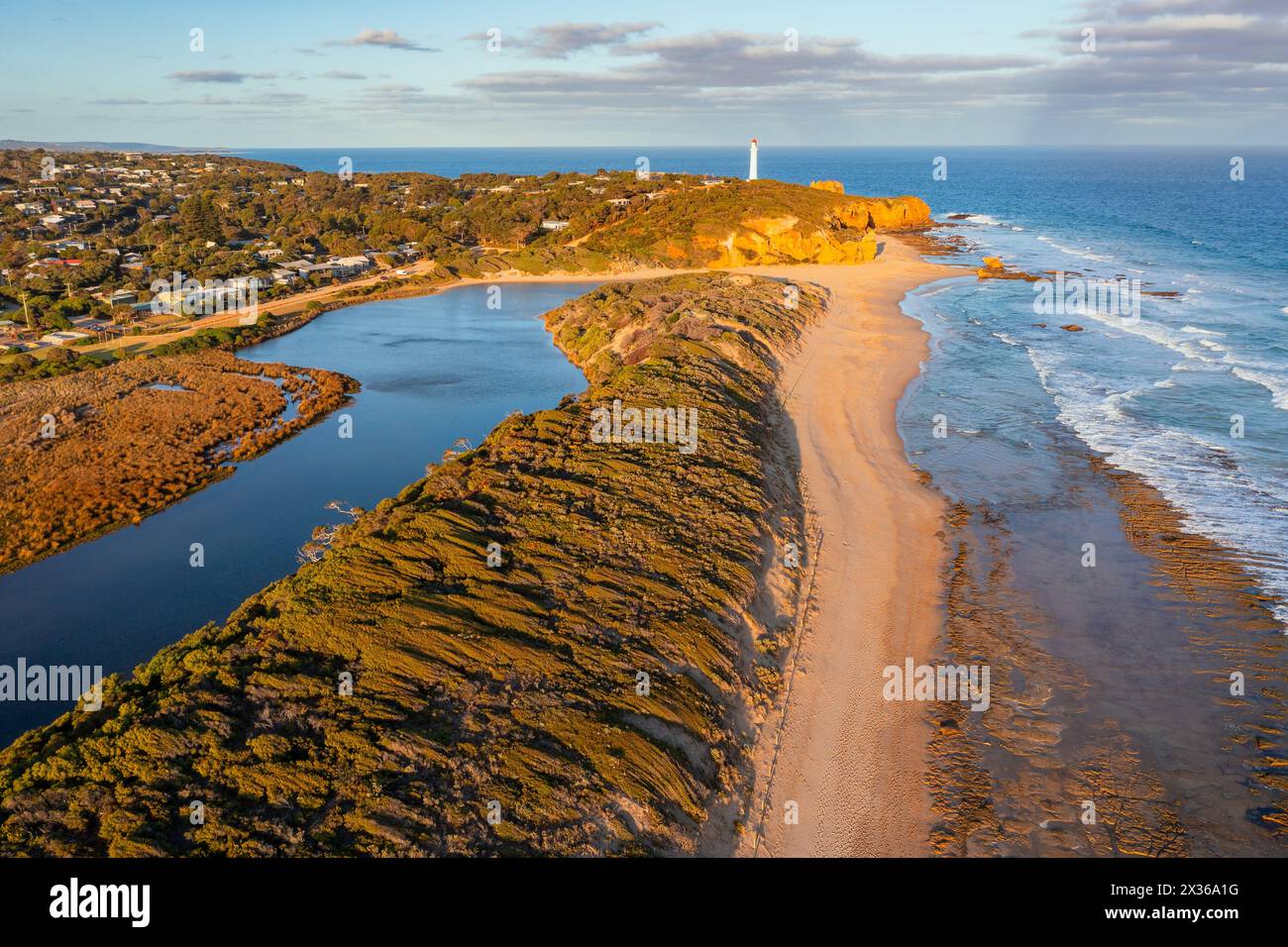 Vue aérienne d'un ruisseau longeant la côte avec un phare lointain à Aireys Inlet sur la Great Ocean Road à Victoria, Australie. Banque D'Images