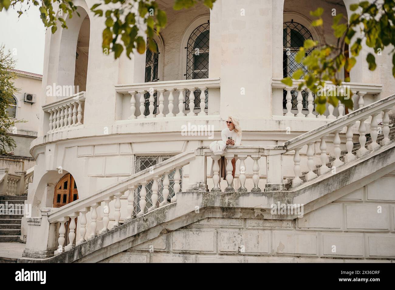 Une femme se tient debout sur le balcon d'un bâtiment avec un chapeau blanc. Le balcon a une rampe et un escalier qui y mène. Banque D'Images