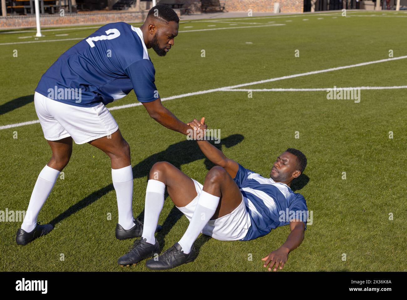 Deux athlètes afro-américains jouent au rugby, l'un aidant l'autre Banque D'Images