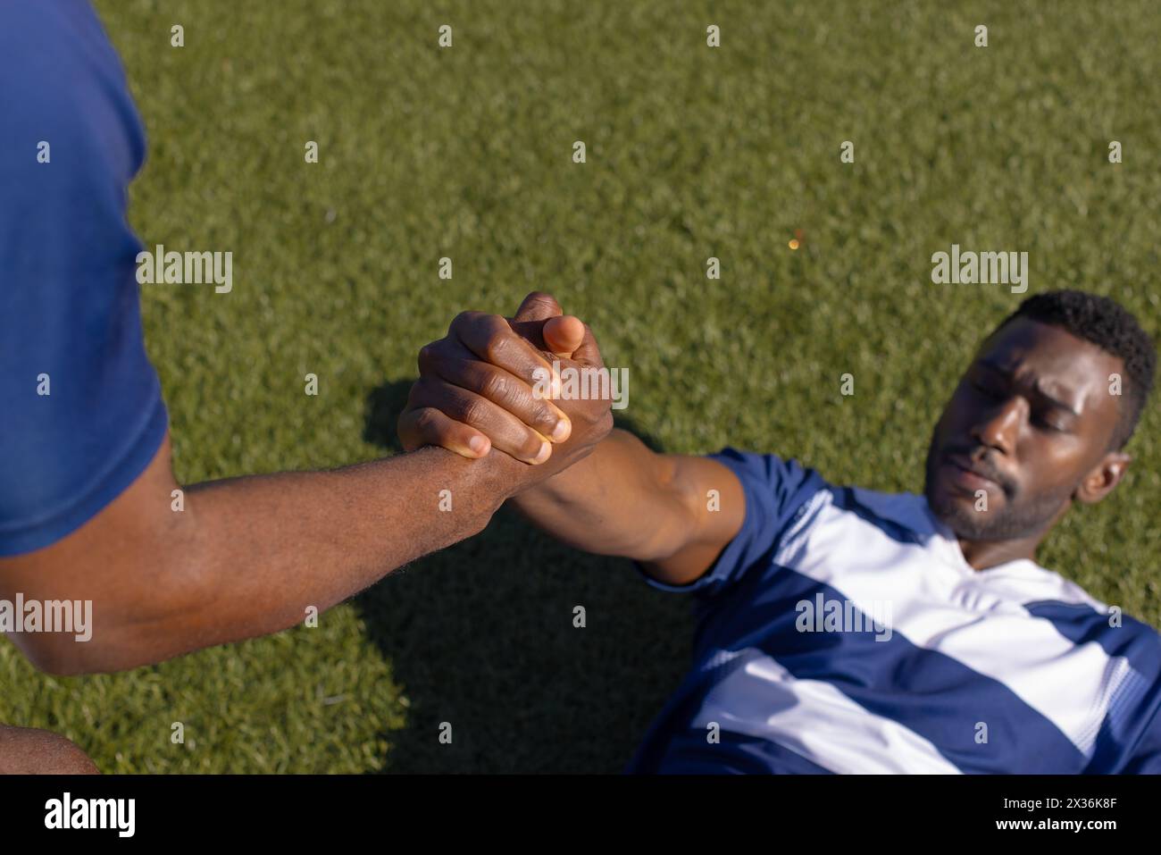 Deux athlètes masculins afro-américains s'entraînent sur un terrain, l'un assiste l'autre à se tenir debout Banque D'Images