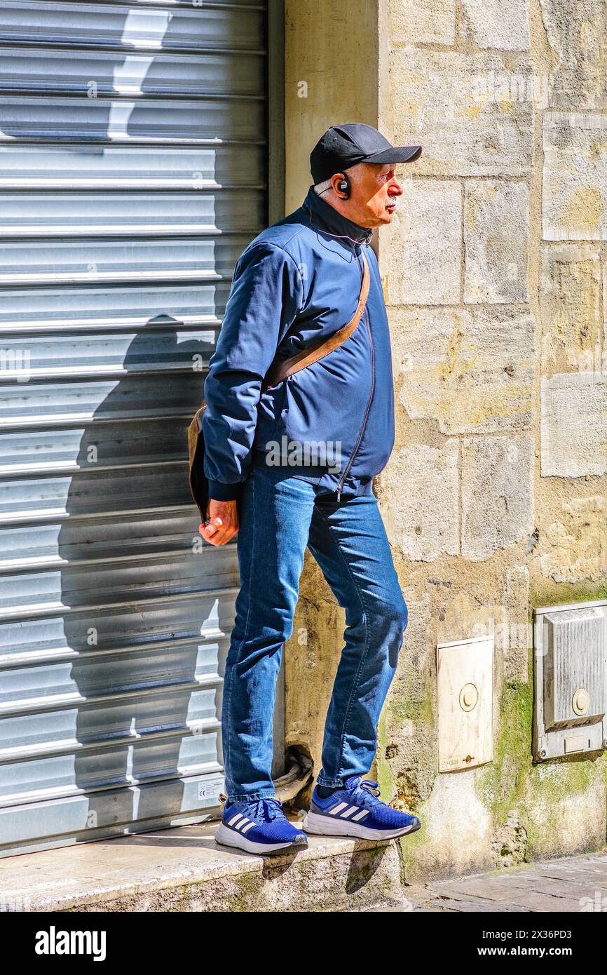 Homme plus âgé vêtu de façon décontractée debout devant des volets fermés en attendant l'ouverture du magasin - Tours, Indre-et-Loire (37), France. Banque D'Images