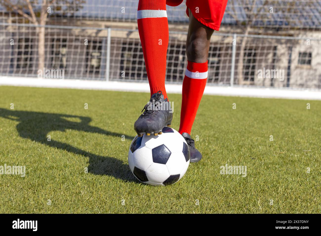 Jeune afro-américain en chaussettes rouges, crampons des marches sur le ballon de football à l'extérieur Banque D'Images