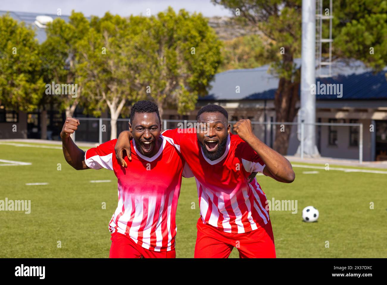 Deux jeunes athlètes afro-américains en maillots rouges célèbrent sur un terrain de football Banque D'Images