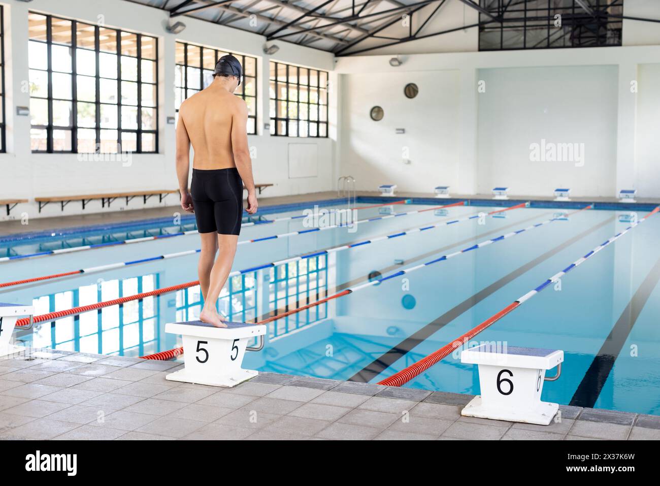 Jeune nageur masculin caucasien debout sur le bloc de départ à la piscine à l'intérieur, espace de copie Banque D'Images