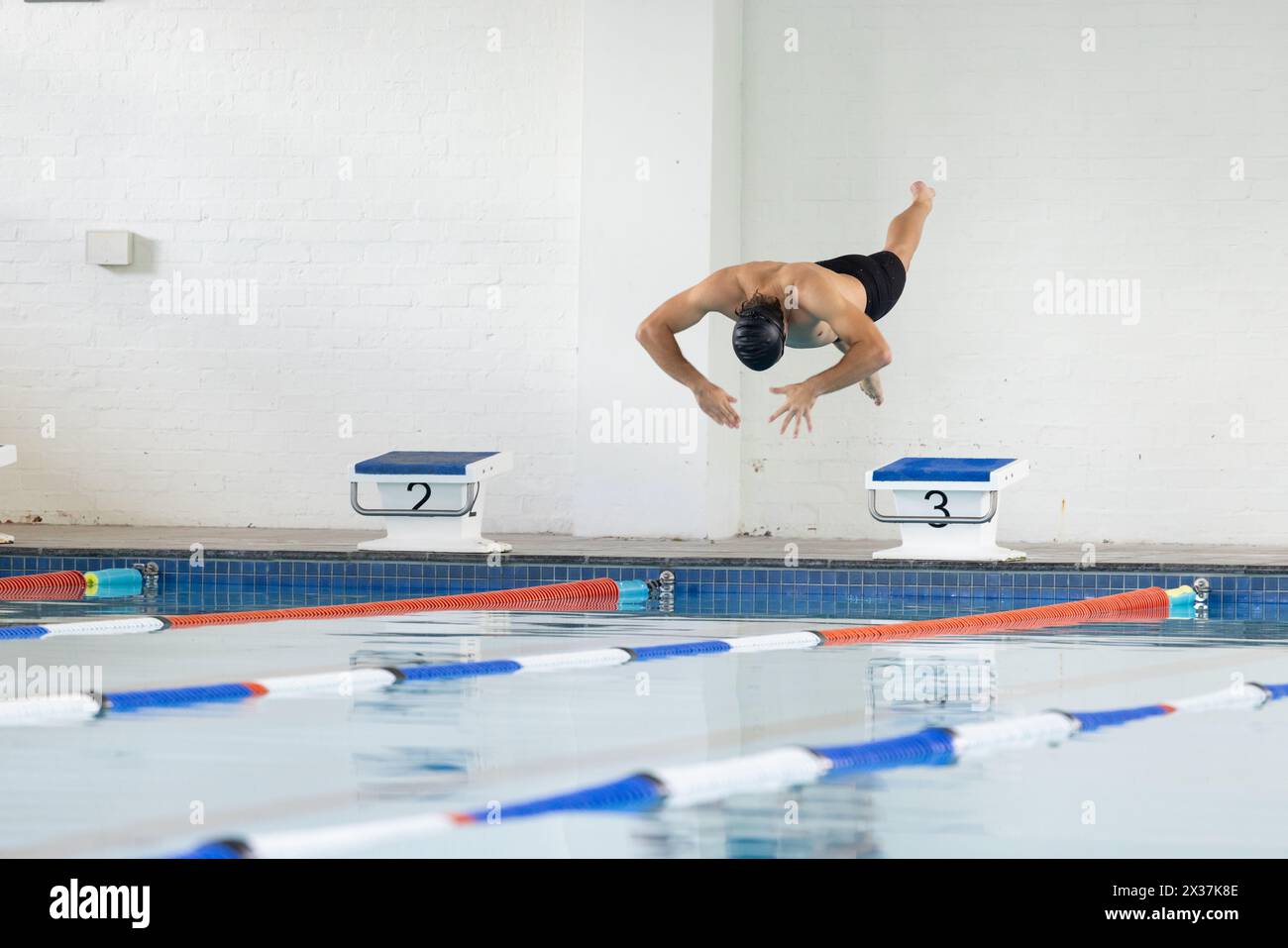Jeune nageur masculin caucasien plongeant dans la piscine intérieure, portant un chapeau noir, espace de copie Banque D'Images