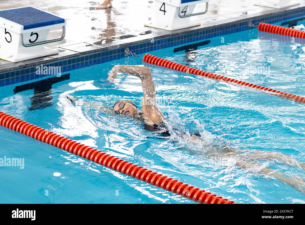 Une jeune nageuse biraciale portant des lunettes, s'entraînant dans une piscine intérieure Banque D'Images