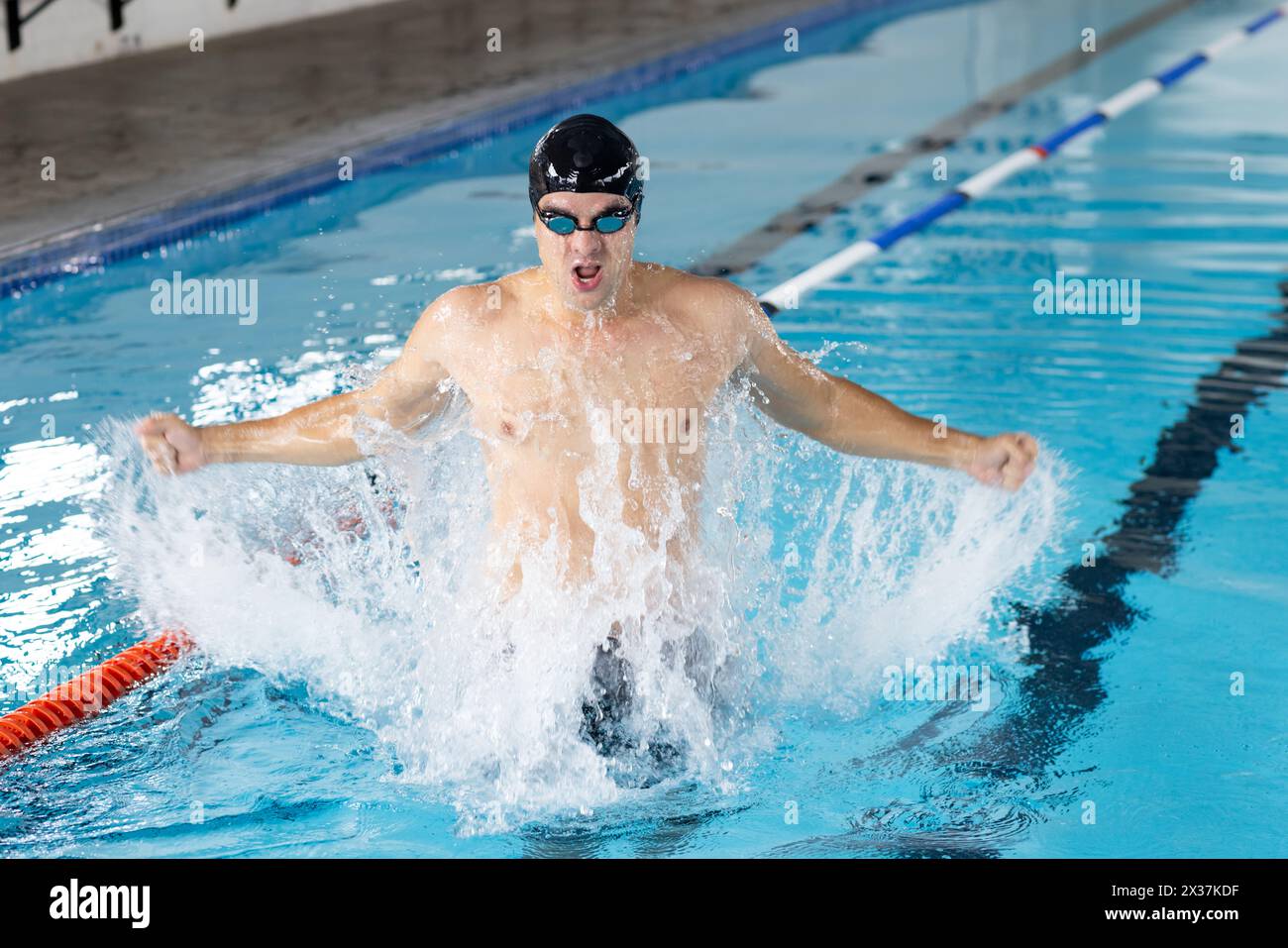Jeune nageur masculin caucasien s'entraînant à l'intérieur dans la piscine, faisant un éclaboussure Banque D'Images